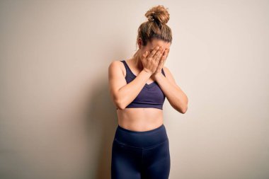 Genç, sarışın, spor yapan, spor giyinen, beyaz arka planda giyinen, ağlarken yüzünü ellerle kapatan genç ve güzel bir bayan. Depresyon kavramı.