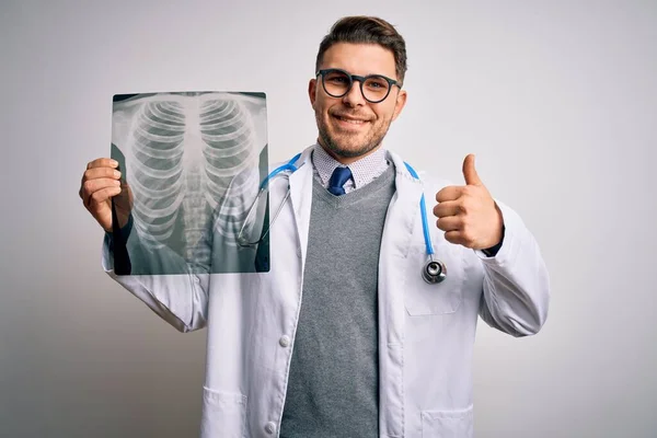 年轻的医生穿着医生的外套 在孤立的背景下看着胸部扫描的放射照片 开心地笑着做着好的手势 用手指竖起大拇指 很好的标志 — 图库照片