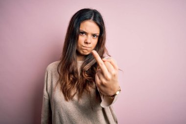 Young beautiful brunette woman wearing casual sweater standing over pink background Showing middle finger, impolite and rude fuck off expression