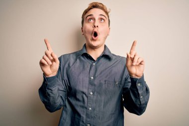 İzole edilmiş beyaz arka plan üzerinde duran genç ve yakışıklı kızıl saçlı adam şaşırmış ve şaşırmıştı. Parmaklarıyla işaret ediyor ve kollarını kaldırıyordu..