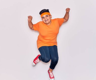 Spor kıyafetleri giyen sevimli İspanyol çocuk mutlu gülümsüyor. İzole edilmiş beyaz arka planda yüzünde gülümsemeyle zıpla