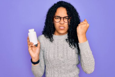 Genç Afro-Amerikalı kıvırcık kadın elinde haplar tutuyordu. Mor arka planda. Sinirli ve sinirli bir şekilde bağırıyordu.