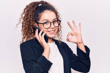 Kıvırcık saçlı, gözlüklü güzel bir kız. Akıllı telefonda konuşuyor. Parmaklarıyla işaret veriyor, gülümsüyor. 