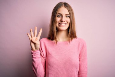 Genç, güzel, kızıl saçlı bir kadın pembe arka planda rahat bir süveter giyiyor. Dört numarayı gösteriyor ve gülümsüyor. Kendinden emin ve mutlu..