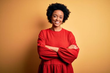 Kıvırcık saçlı, rahat kazak giyen, kollarını kavuşturup kameraya gülümseyen güzel Afro-Amerikan kadın. Pozitif kişi.