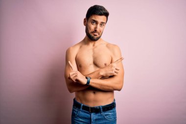 Genç, yakışıklı, sakalsız, pembe arka planda duran, her iki tarafı da parmaklarıyla işaret eden, farklı yönlü, sakallı, güçlü bir adam.