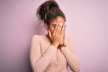 Genç, güzel, Afro-Amerikalı bir kız pembe arka planda dikilmiş ağlarken suratını ellerle kapatan sıradan bir süveter giyiyor. Depresyon kavramı.