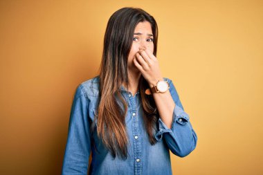 Genç, güzel bir kız, izole edilmiş sarı arka planda dikilmiş sıradan bir kot gömlek giyiyor. Kokuşmuş, iğrenç, dayanılmaz bir koku alıyor. Parmakları burnunda nefesini tutuyor. Kötü kokuyor.