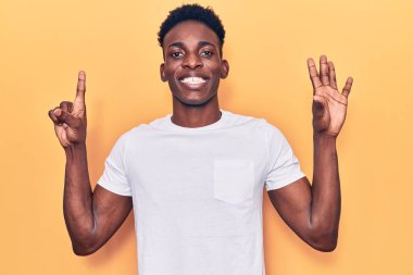 Genç Afro-Amerikalı günlük kıyafetler giymiş altı numarayı gösterip işaret ederken kendinden emin ve mutlu bir şekilde gülümsüyor.. 