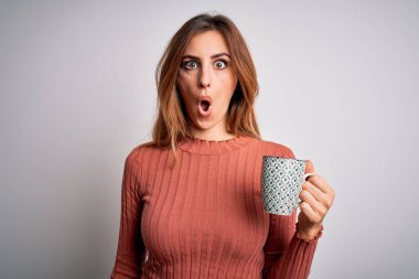 Genç, güzel esmer kadın izole edilmiş beyaz arka planda bir fincan kahve içiyor. Şaşırmış bir yüz ifadesinden korkuyor ve heyecanlanıyor.