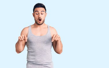 Mayo giyen ve kolsuz tişört giyen genç yakışıklı adam parmaklarını göstererek reklamını yapıyor, şaşırmış yüz ve ağzını açıyor. 