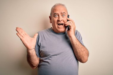 Orta yaşlı, ağlak bir adam beyaz arka planda telefonla konuşuyor. Çok mutlu ve heyecanlı, kazanan yüz ifadesi zaferi büyük bir gülümsemeyle kutluyor ve ellerini kaldırıyor.