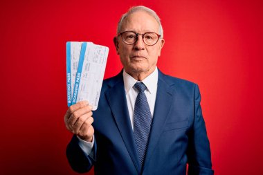 Senior grey haired business man holding airplane boarding pass over red background with a confident expression on smart face thinking serious clipart