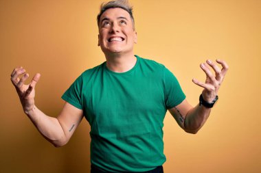 Sarı arka plan üzerine gündelik yeşil tişört giyen genç, yakışıklı ve modern bir adam deli gibi bağırıyor ve agresif bir ifade ve kollarla bağırıyor. Hayal kırıklığı konsepti.