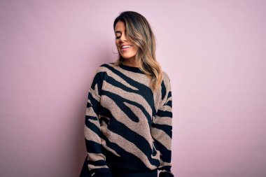 Moda kıyafetleri giyen genç ve güzel bir kadın. Manken, sokak tarzı giyiniyor. Pembe arka planda dikiliyor.