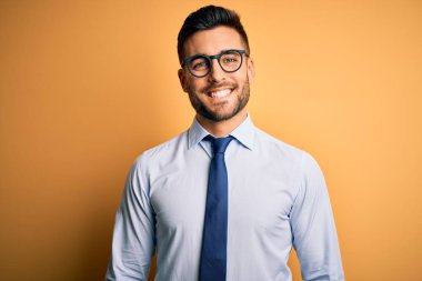 Sarı arka plan üzerinde mutlu ve havalı bir gülümseme ile duran kravat ve gözlük takan genç yakışıklı iş adamı. Şanslı kişi..
