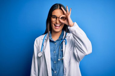 Mavi arka planda steteskop ve gözlük takan genç, güzel bir doktor el hareketleriyle gülümsüyor ve mutlu yüzle parmaklarından bakıyor..