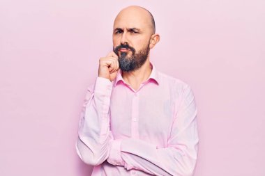 İş kıyafetleri giymiş yakışıklı bir genç adam ciddi bir yüz ifadesi, eli çenesinde soru soran, kafa karıştırıcı bir fikir hakkında düşünceli. 