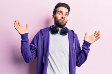 Sakallı, müzik dinleyen, kulaklık takan ve kolları açık, kafası karışık genç yakışıklı bir adam.. 