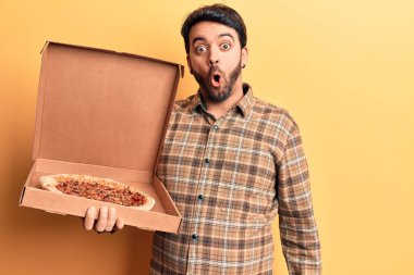 İspanyol genç adam elinde pizza kutusu tutuyor. Korkmuş ve ağzı açık kalmış, şaşırmış ve şaşırmış. 