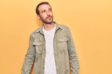 Gündelik giysiler giymiş genç yakışıklı bir adam yüzünde gülümsemeyle yan yana bakıyor, doğal bir ifade. Kendinden emin gülen. 