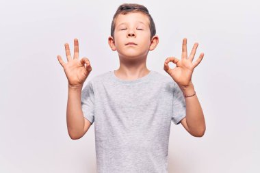 Hoş sarışın çocuk günlük kıyafetler giyip rahatlıyor ve gözleri kapalı gülümsüyor parmaklarıyla meditasyon hareketi yapıyor. yoga konsepti. 