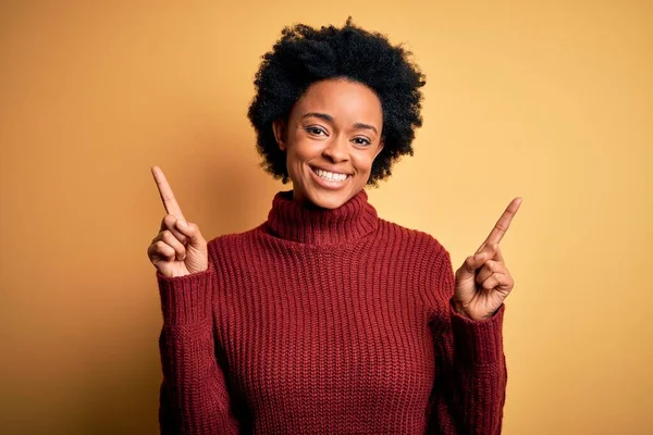 巻き毛のある若い美しいアフリカ系アメリカ人アフロ女性は さまざまな方向に指で自信を持って指して笑顔カジュアルなタートルネックセーターを着ています 広告のコピースペース — ストック写真