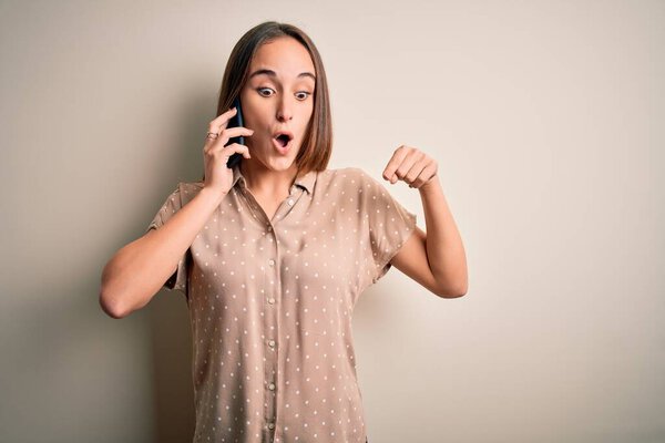 Young beautiful woman having conversation talking on the smartphone over white background Pointing down with fingers showing advertisement, surprised face and open mouth