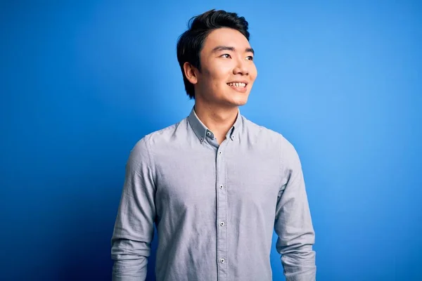 若いハンサムな中国人男性が孤立した青の背景に離れて顔に笑顔で側に見て立ってカジュアルなシャツを着て 自然な表情 自信を持って — ストック写真