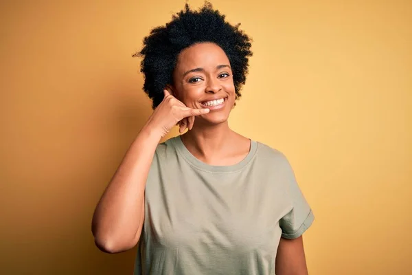 カジュアルなTシャツを着た巻き毛をした若い美しいアフリカ系アメリカ人アフロ女性は 電話で話すような手や指で電話のジェスチャーをして笑っています 概念の伝達 — ストック写真
