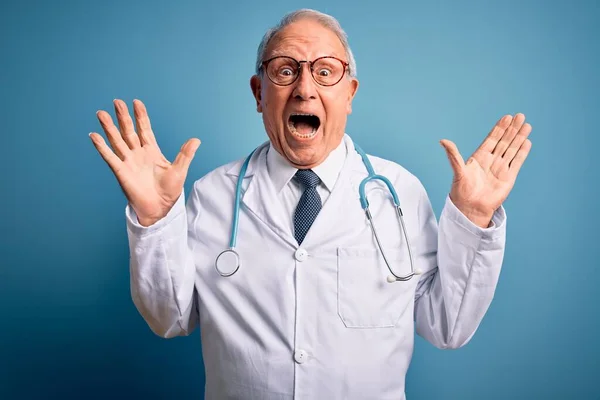 Starszy Siwowłosy Lekarz Noszący Stetoskop Płaszcz Medyczny Niebieskim Tle Świętujący — Zdjęcie stockowe