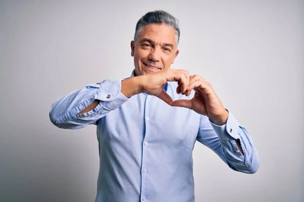 Middle age handsome grey-haired business man wearing elegant shirt over white background smiling in love doing heart symbol shape with hands. Romantic concept.