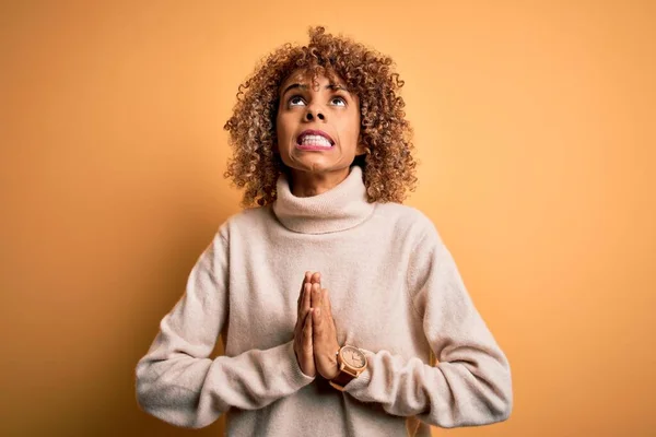 Young beautiful african american woman wearing turtleneck sweater over yellow background begging and praying with hands together with hope expression on face very emotional and worried. Begging.