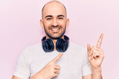 Genç yakışıklı kel adam müzik dinliyor kulaklıkla gülümsüyor ve kameraya bakıyor iki eliyle ve parmaklarıyla kenarı işaret ediyor.. 