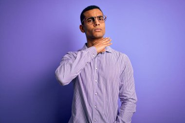 Yakışıklı Afro-Amerikan erkeği çizgili gömlek ve gözlük takıyor mor arka planda boğazı bıçak gibi kesiyor, saldırganlığı şiddetli bir şiddetle tehdit ediyor.