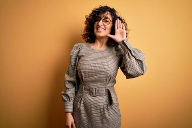 Güzel bir Arap iş kadını. Elbise ve gözlük takıyor. Sarı arka planda duruyor.