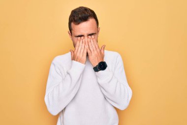 Mavi gözlü, sıradan bir süveter giyen, sarı arka planda duran, yorgunluk ve baş ağrısı için gözlerini ovuşturan, uykulu ve yorgun yüzlü genç bir adam. Görüş sorunu