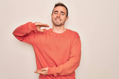 Mavi gözlü genç bir adam beyaz arka plan üzerinde dikilmiş büyük ve büyük boyut işareti, ölçü sembolü gösteren el kol hareketi yapıyor. Kameraya bakıp gülümsüyor. Ölçüm konsepti.