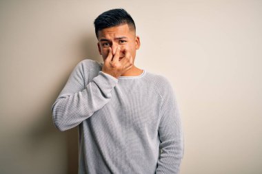 İzole edilmiş beyaz arka planda dikilen gündelik süveter giyen genç, yakışıklı latin adam pis ve iğrenç bir koku alıyor. Nefesini burnunda tutuyor. Kötü kokuyor.