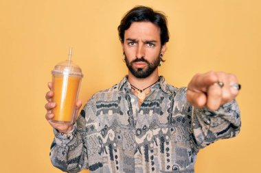 Yakışıklı İspanyol asıllı bohem hippi ayı sağlıklı taze portakal suyu içiyor. Kamerayı işaret ediyor ve sen, el işareti, ön taraftan pozitif ve kendinden emin bir hareket.
