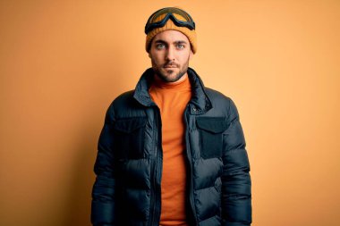 Kar giysileri ve kayak gözlüğü takan sakallı yakışıklı kayakçı yüzünde ciddi bir ifadeyle rahatladı. Basit ve doğal bir şekilde kameraya bakıyorsun..