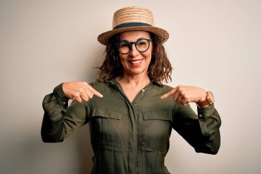 Orta yaşlı esmer kadın, gözlüklü ve şapkalı. İzole edilmiş beyaz arka planda duruyor. Kendine güvenen, gülümseyen, kendini gururlu ve mutlu gösteren biri..