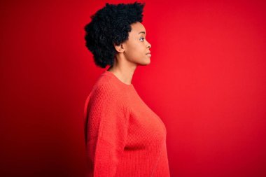 Kıvırcık saçlı, sıradan bir süveter giyen, rahat bir profil pozu veren, kendine güvenen gülümseyen güzel Afro-Amerikan kadın..