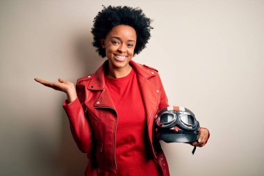 Kıvırcık saçlı, motosiklet kasklı, neşeli gülümseyen, avuç içi kameraya bakan Afro-Amerikan motosikletli genç bir kadın..