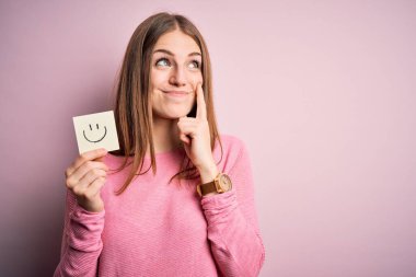 Genç, güzel, kızıl saçlı kadın elinde gülümseyen bir kâğıt tutuyordu. Emoji mesajı. Ciddi bir yüz ifadesi vardı.