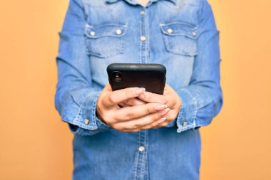 Genç beyaz kadın, izole edilmiş sarı arka plan üzerinde akıllı telefon kullanarak konuşuyor.