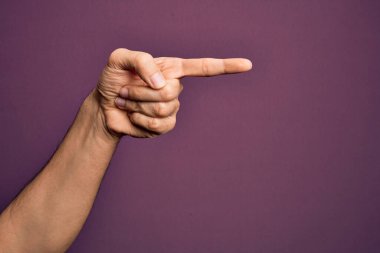 İzole edilmiş mor arka plan üzerinde parmaklarını gösteren beyaz bir gencin eli işaret parmağıyla kenarı işaret ediyor ve bir seçim yapıyor.