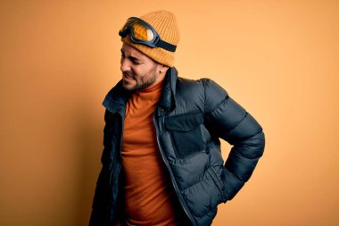 Kar giysileri ve kayak gözlüğü takan yakışıklı kayakçı adam sırt ağrısı çekiyor, elleriyle dokunuyor, kas ağrısı çekiyor.