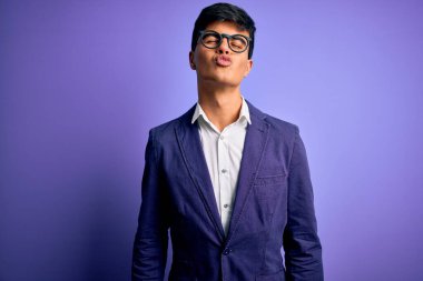 Ceket ve gözlük takan yakışıklı genç bir iş adamı mor arka planda kameraya bakıp havada öpüşürken güzel ve seksi görünüyor. Aşk ifadesi.