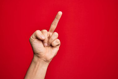 Hand of caucasian young man showing fingers over isolated red background showing provocative and rude gesture doing fuck you symbol with middle finger